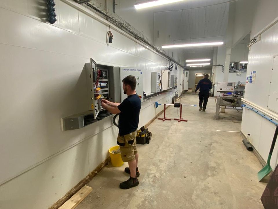 GDL engineer wiring a wall-mounted control panel beside a spinner control panel in a hatchery